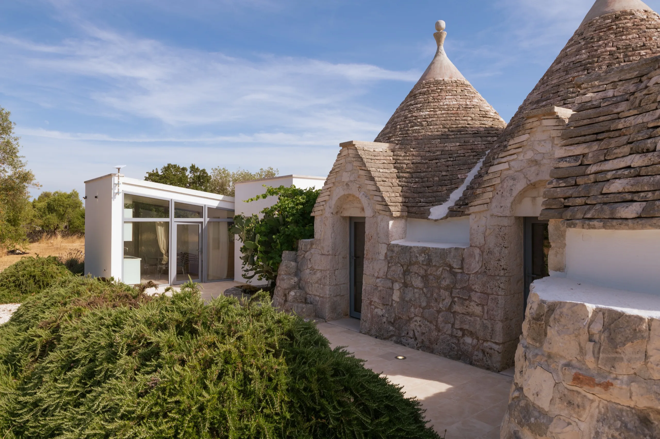 L’extension contemporaine vitrée et les trulli de pierre côte à côte